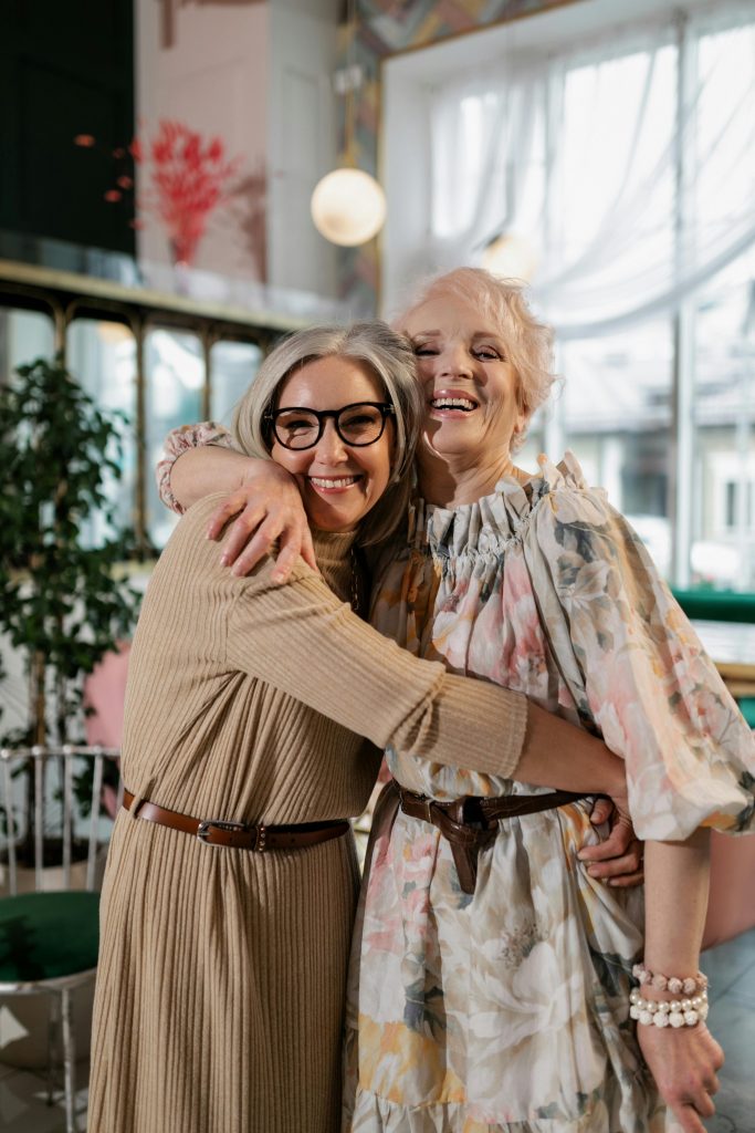 Two senior women hugging joyfully indoors, showcasing friendship and happiness.